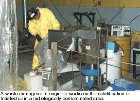 A waste mangement engineer works on the solidification of tritiated oil in a radiologicaly contaminated area.